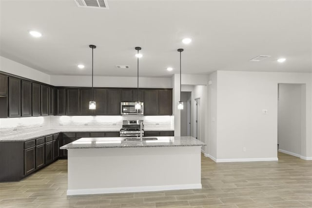 18309 Emu Ln, Manor, TX 78653 - kitchen with stainless steel appliances, a sink, light stone counters, a kitchen island with sink, and dark brown cabinets