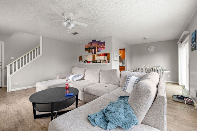 living area with a textured ceiling, visible vents, stairs, ceiling fan, and light wood-style floors