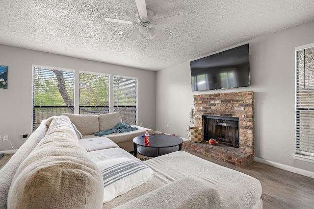 living area featuring baseboards, wood finished floors, ceiling fan, and a brick fireplace