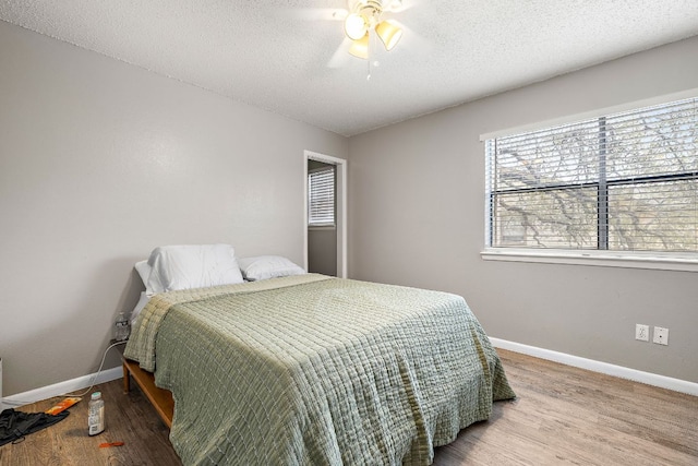 bedroom with a ceiling fan, a textured ceiling, baseboards, and wood finished floors