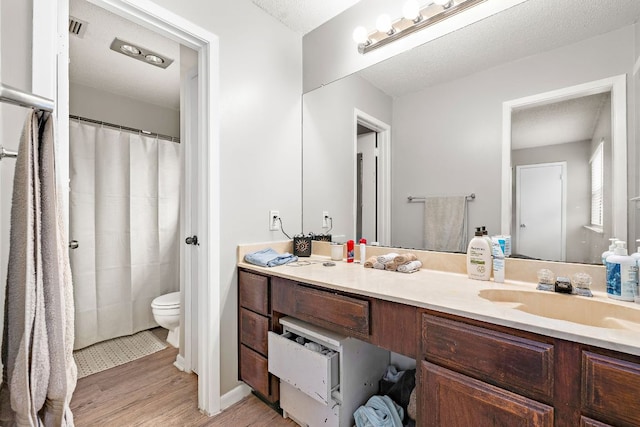full bathroom with vanity, toilet, a textured ceiling, visible vents, and wood finished floors