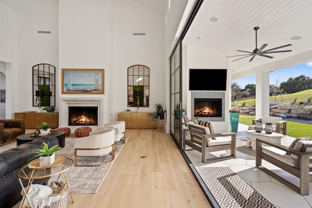 living room featuring ceiling fan, a lit fireplace, and a towering ceiling