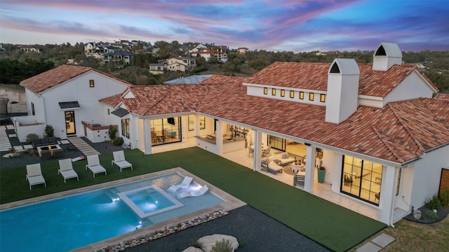 back of house at dusk featuring stucco siding, outdoor lounge area, a patio area, and a lawn