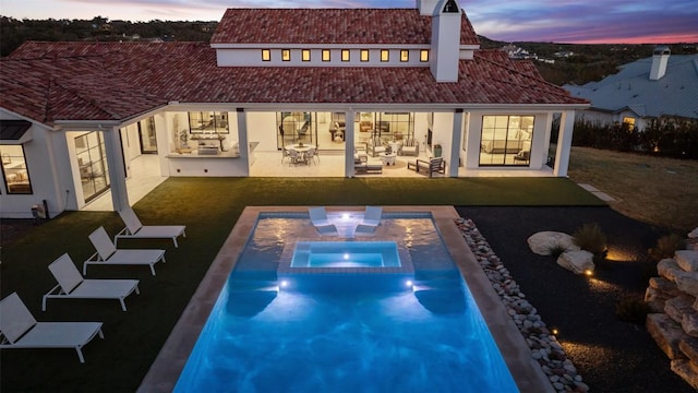 back of house at dusk with stucco siding, a patio area, and a lawn
