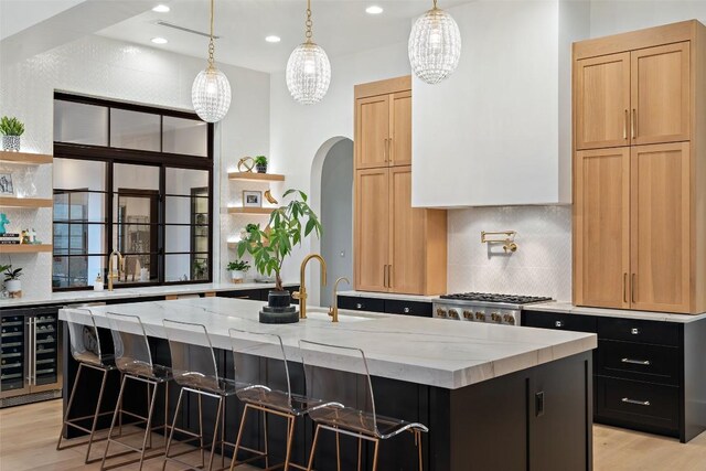 kitchen with open shelves, backsplash, light stone counters, and a center island with sink
