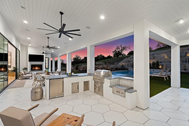 view of patio / terrace featuring grilling area, a warm lit fireplace, outdoor wet bar, and area for grilling