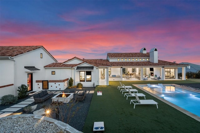 rear view of property with a patio area, an outdoor kitchen, an outdoor living space with a fire pit, and stucco siding