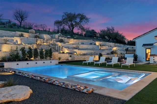 pool at dusk with a pool with connected hot tub and a lawn