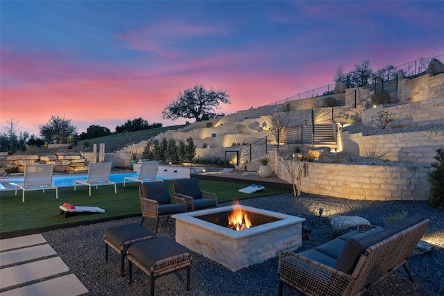 patio terrace at dusk with a fire pit, a yard, and stairs