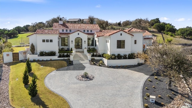 mediterranean / spanish-style home featuring a tile roof, a chimney, stucco siding, and curved driveway