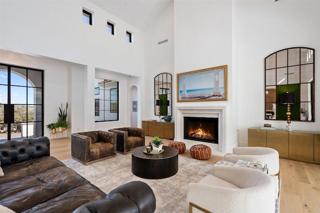 living room with arched walkways, light wood-style flooring, a towering ceiling, and a lit fireplace
