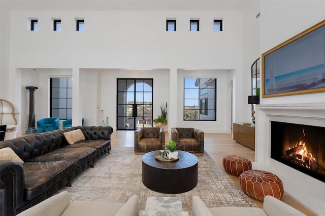 living area with a high ceiling, a lit fireplace, and wood finished floors