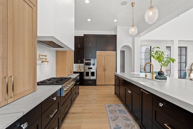 kitchen featuring a sink, light wood-style flooring, tasteful backsplash, appliances with stainless steel finishes, and custom range hood