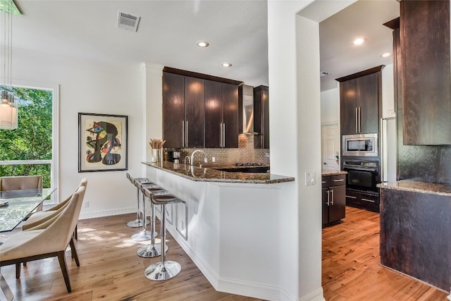5802 Gentle Breeze Ter, Austin, TX 78731 - kitchen with black oven, stainless steel microwave, dark stone countertops, decorative backsplash, and a kitchen breakfast bar