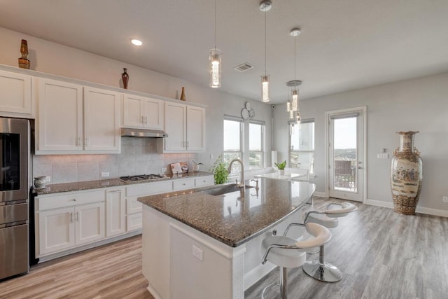 1304 Positano Pass, Leander, TX 78641 - kitchen with a sink, stainless steel appliances, under cabinet range hood, white cabinetry, and dark stone countertops