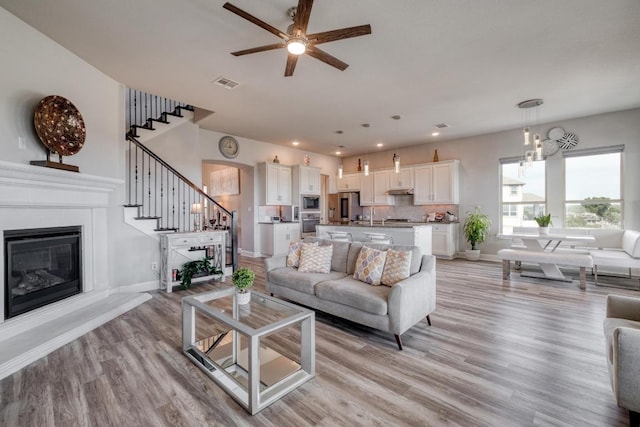 1304 Positano Pass, Leander, TX 78641 - living room with a glass covered fireplace, stairs, a ceiling fan, light wood-style flooring, and recessed lighting