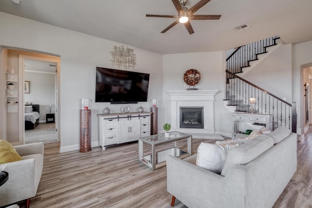1304 Positano Pass, Leander, TX 78641 - living room featuring a ceiling fan, wood finished floors, stairs, a glass covered fireplace, and baseboards