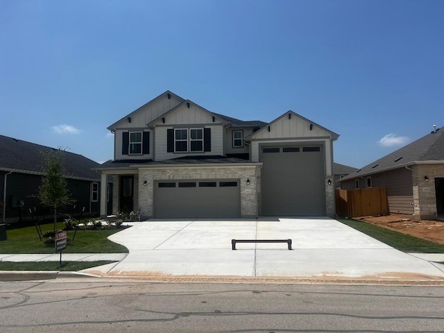 craftsman-style house featuring board and batten siding, driveway, a garage, fence, and stone siding