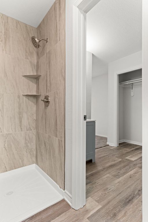 full bath with baseboards, wood finished floors, and tiled shower