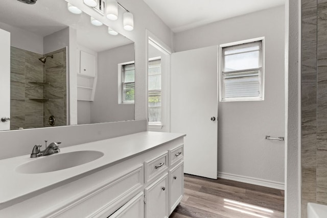 bathroom featuring vanity, baseboards, tiled shower, and wood finished floors