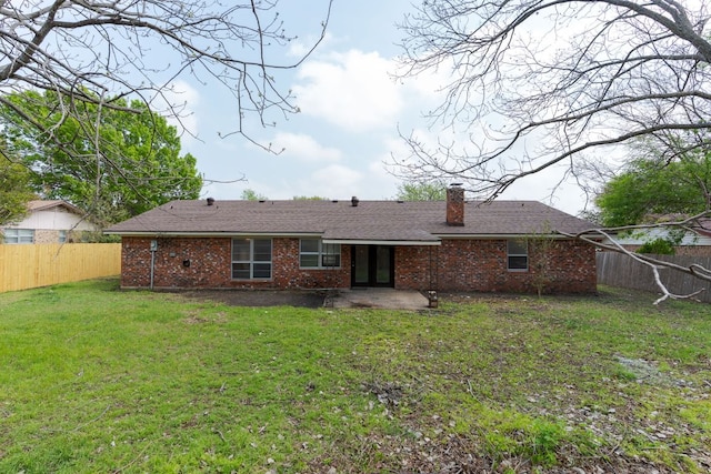 rear view of house featuring a patio, a chimney, a fenced backyard, brick siding, and a lawn