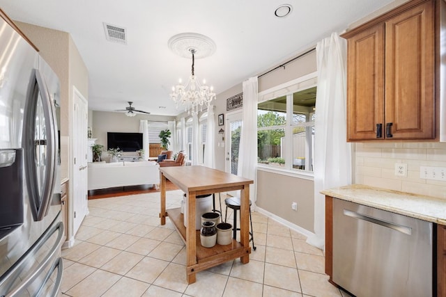 105 Wimberley St, Hutto, TX 78634 - kitchen with appliances with stainless steel finishes, light tile patterned floors, brown cabinets, ceiling fan, and a chandelier