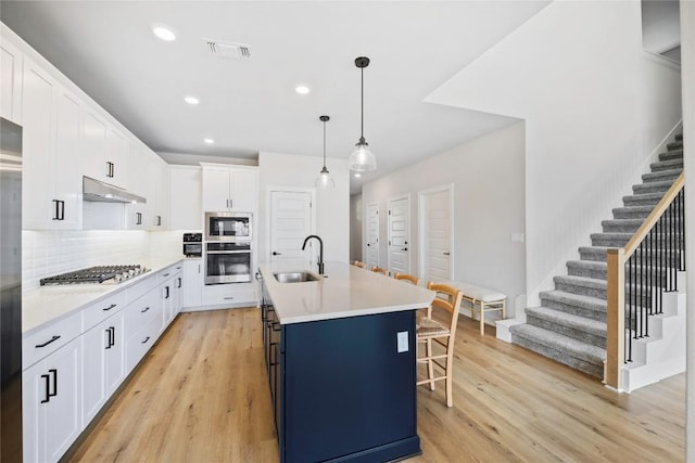 1017 Dog Iron St, Georgetown, TX 78633 - kitchen featuring stainless steel appliances, under cabinet range hood, white cabinetry, light wood finished floors, and recessed lighting