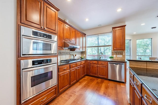 7724 Yaupon Dr, Austin, TX 78759 - kitchen featuring stainless steel appliances, brown cabinets, a sink, light wood finished floors, and under cabinet range hood