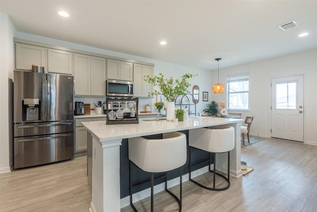 12305 Zenyatta Dr, Buda, TX 78610 - kitchen with a breakfast bar area, visible vents, appliances with stainless steel finishes, gray cabinetry, and light wood-style floors