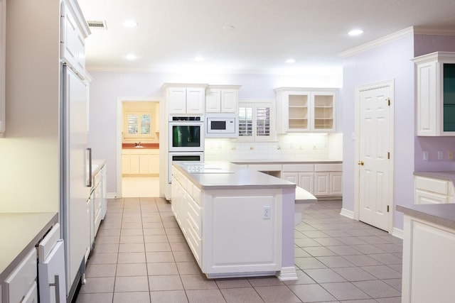kitchen with white cabinetry, tasteful backsplash, crown molding, white appliances, and a kitchen island