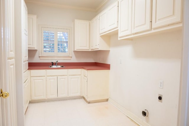 kitchen featuring ornamental molding, baseboards, a sink, white cabinets, and light floors