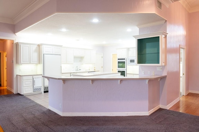 kitchen featuring a breakfast bar area, a peninsula, white appliances, visible vents, and ornamental molding