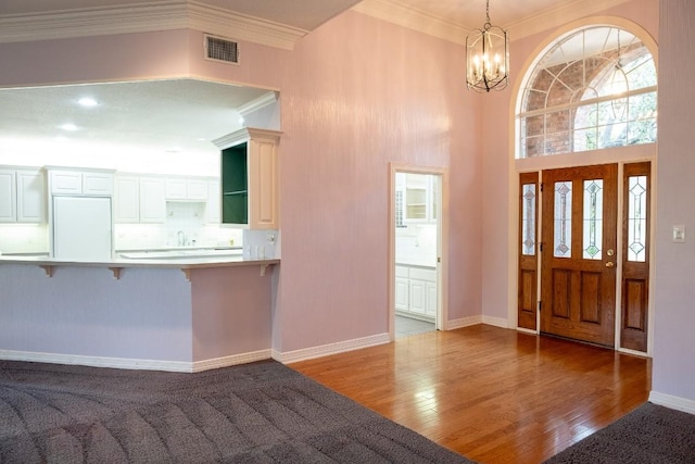 foyer featuring ornamental molding, baseboards, a chandelier, visible vents, and wood finished floors
