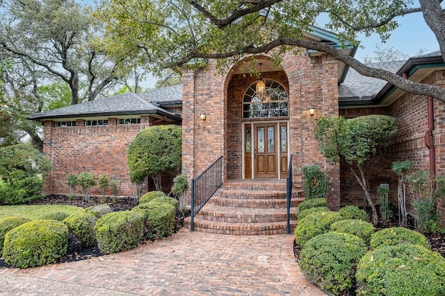 property entrance featuring french doors, a shingled roof, and brick siding