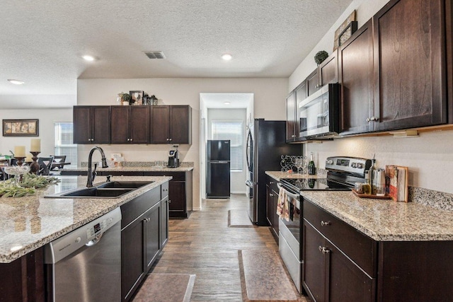 759 Ocelot Ct, Seguin, TX 78155 - kitchen featuring stainless steel appliances, dark brown cabinets, wood finished floors, a textured ceiling, and a kitchen island with sink