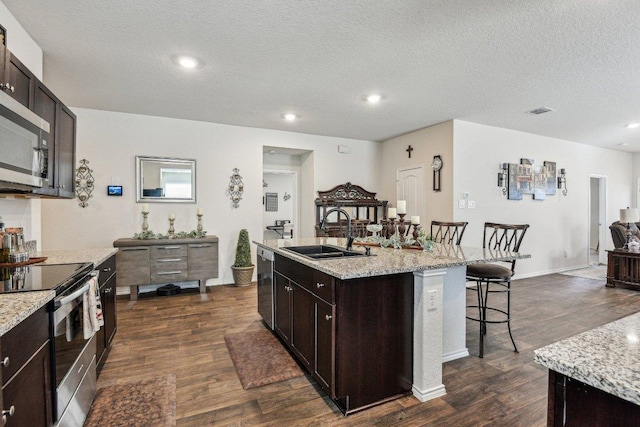 759 Ocelot Ct, Seguin, TX 78155 - kitchen featuring appliances with stainless steel finishes, a kitchen breakfast bar, dark wood-style flooring, an island with sink, and dark brown cabinets