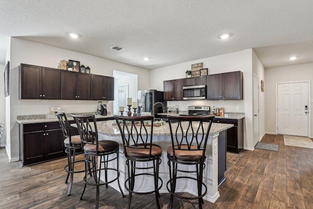 759 Ocelot Ct, Seguin, TX 78155 - kitchen featuring appliances with stainless steel finishes, a breakfast bar, dark brown cabinets, dark wood-style flooring, and a textured ceiling