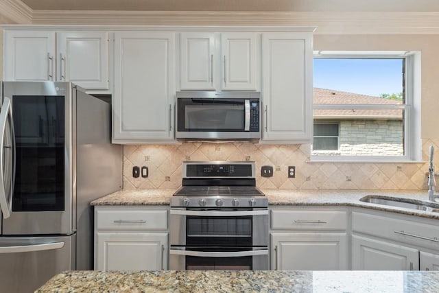 kitchen featuring light stone counters, white cabinetry, a sink, stainless steel appliances, and backsplash