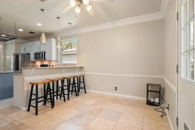 kitchen featuring a kitchen bar, tasteful backsplash, crown molding, a ceiling fan, and appliances with stainless steel finishes