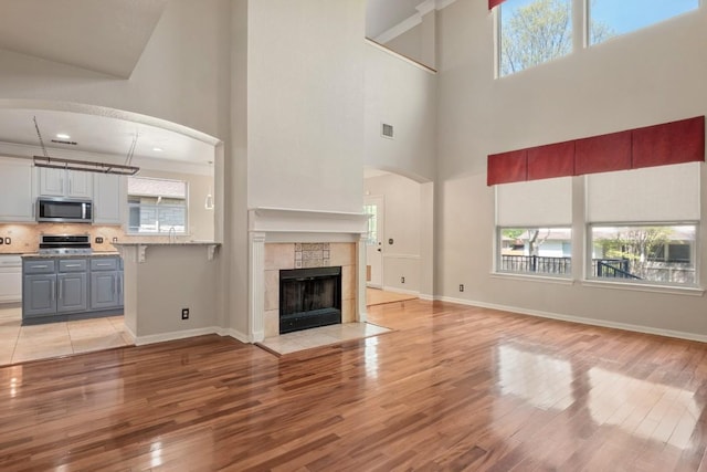 unfurnished living room featuring a tile fireplace, visible vents, light wood-style flooring, and a high ceiling