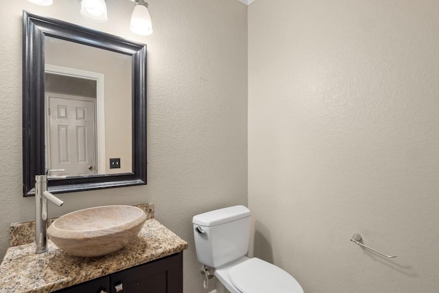 bathroom with toilet, a textured wall, and vanity