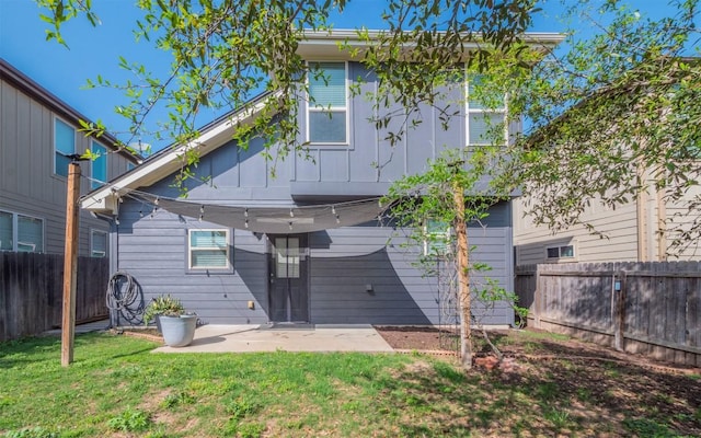 rear view of house with a fenced backyard, board and batten siding, a yard, and a patio area