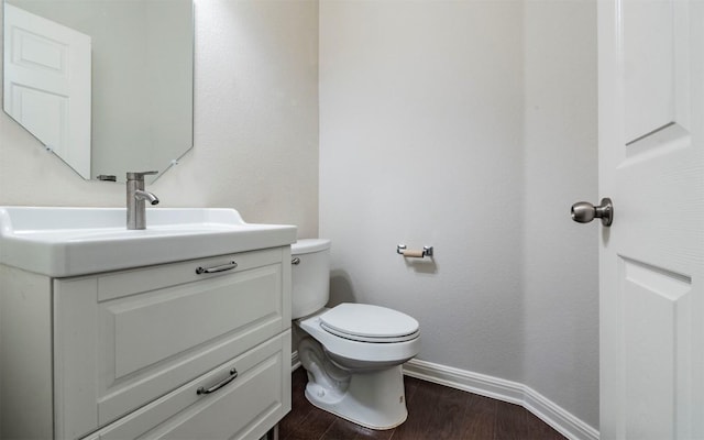 half bath featuring toilet, vanity, baseboards, and wood finished floors