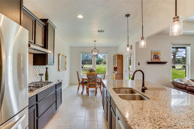 334 Sapling Dr, Driftwood, TX 78619 - kitchen with freestanding refrigerator, backsplash, under cabinet range hood, stainless steel gas cooktop, and decorative light fixtures