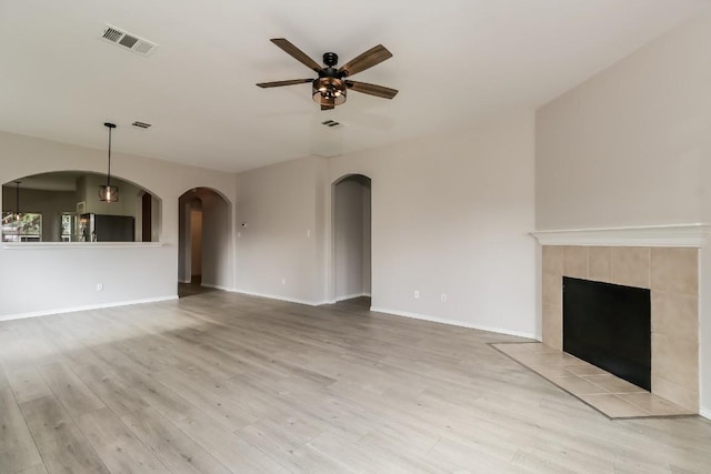 unfurnished living room featuring a ceiling fan, arched walkways, baseboards, visible vents, and light wood-style floors