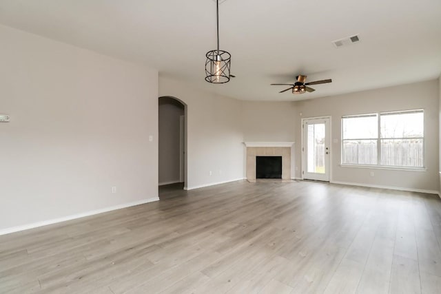 unfurnished living room with light wood-type flooring, arched walkways, visible vents, a ceiling fan, and a tile fireplace