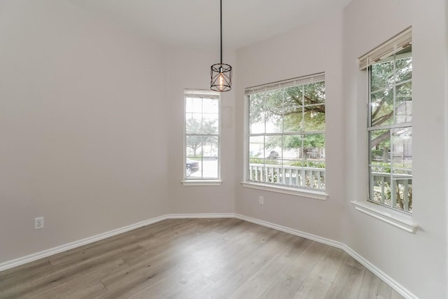 spare room with light wood-style flooring, a notable chandelier, and baseboards