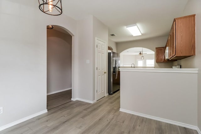 kitchen with arched walkways, brown cabinetry, stainless steel fridge, and light wood-style floors