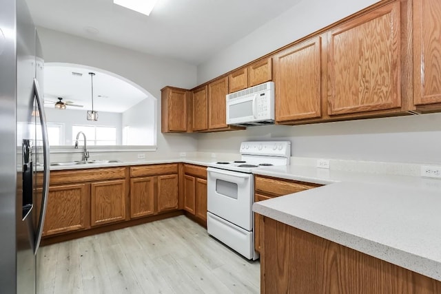 kitchen featuring white appliances, brown cabinetry, light wood-style flooring, and a sink