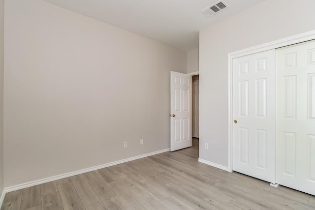 unfurnished bedroom with light wood-style flooring, a closet, baseboards, and visible vents